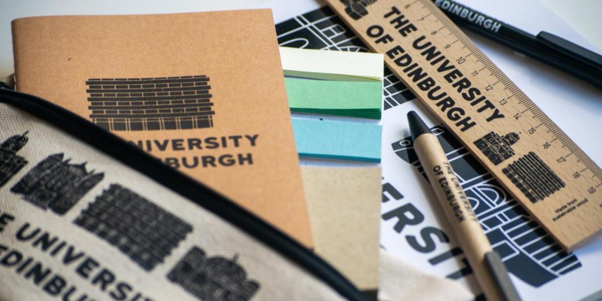 A selection of University of Edinburgh merchandise including pens, notebooks and a ruler spread across a table.
