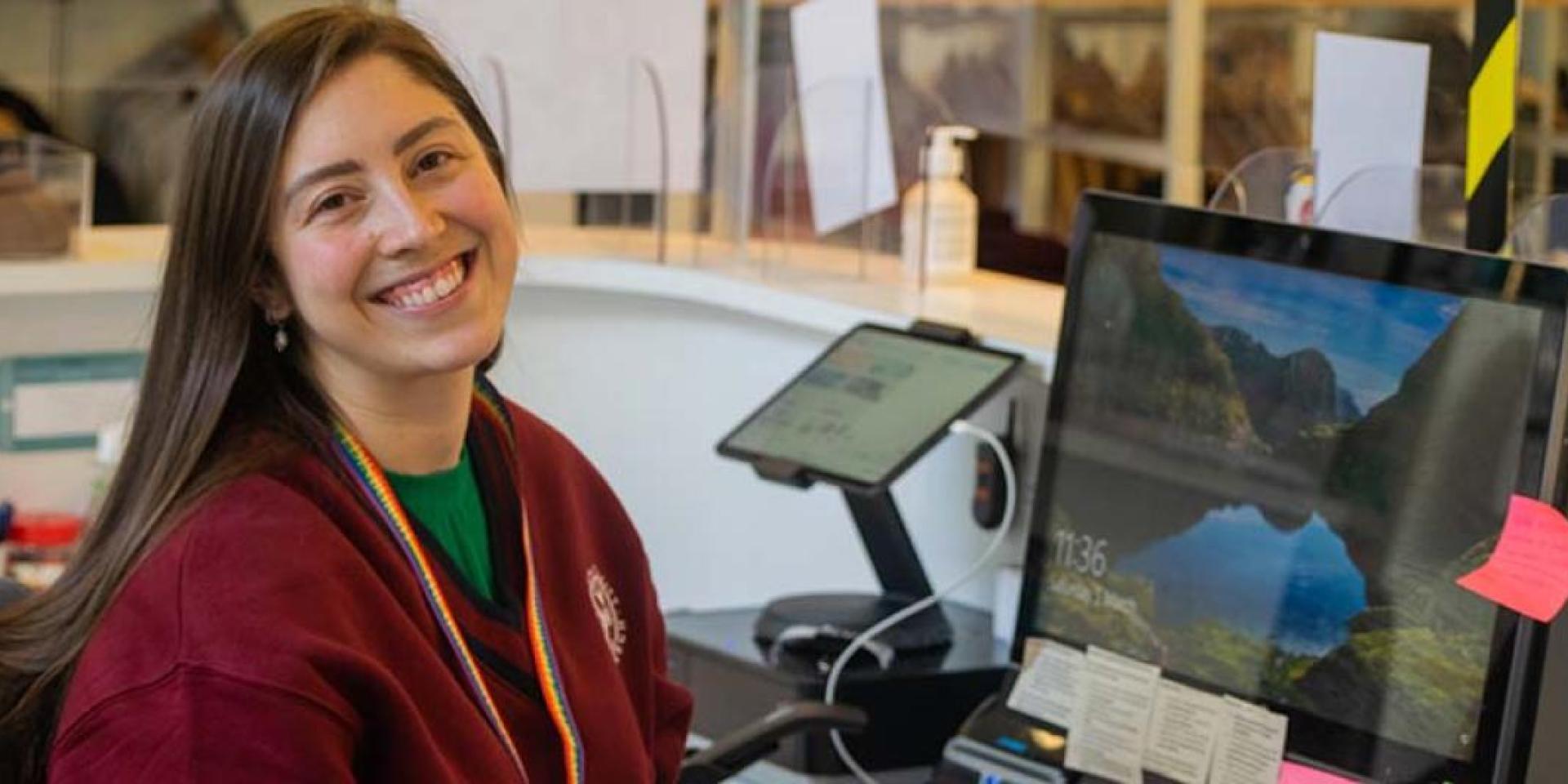 A staff member smiles to camera while working at a desk in The University Of Edinburgh Visitor Centre