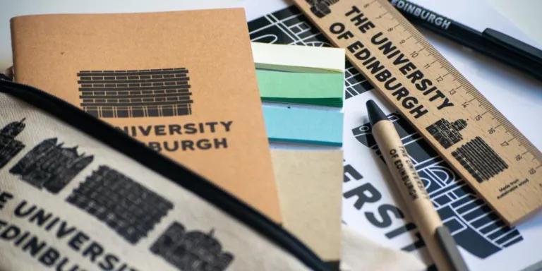 A selection of University of Edinburgh merchandise including pens, notebooks and a ruler spread across a table.
