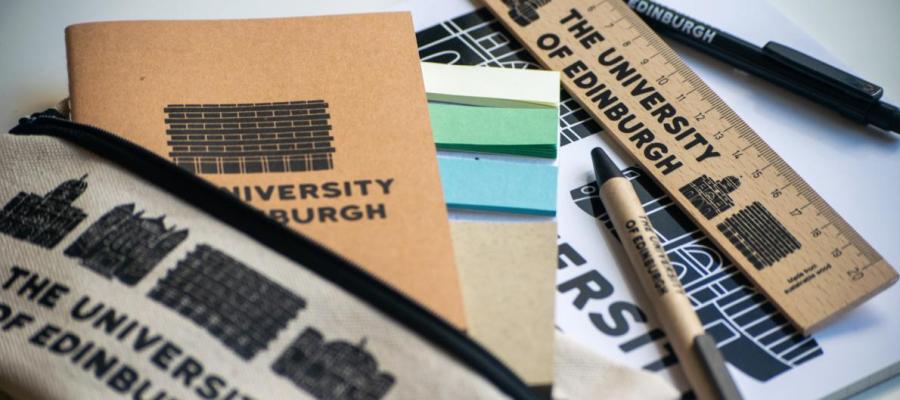 A selection of University of Edinburgh merchandise including pens, notebooks and a ruler spread across a table.