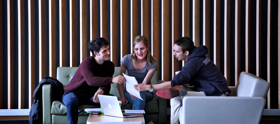 Image shows three students sitting around a table engaging in conversation.