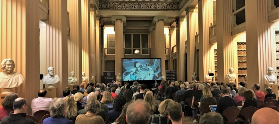 Image shows a seated crowd watching a video demonstration.