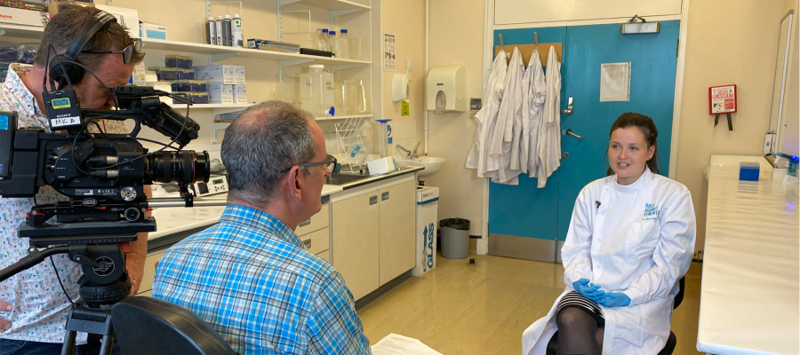 Image shows a medical professional being interviewed with the cameraman and interviewer visible.